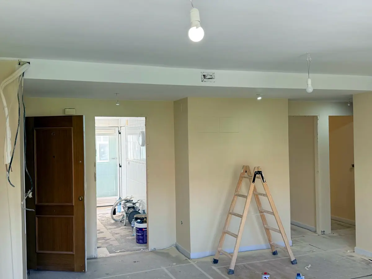 Pintor trabajando en un salón con el suelo protegido durante la obra de pintura